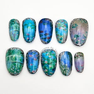 May include: A set of ten artificial nails with a water lily design. The nails feature a variety of blue, green, and purple hues, with a silver metallic border. The design is reminiscent of a Monet painting.