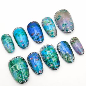 May include: A set of ten artificial nails with a water lily design. Each nail features a different section of a water lily pond, with blue, green, and purple hues. The nails are outlined with a silver metallic trim.