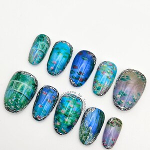 May include: A set of ten artificial nails with a water lily design. The nails are oval-shaped and feature a silver metallic trim. The artwork includes shades of blue, green, and pink, resembling a Monet painting.