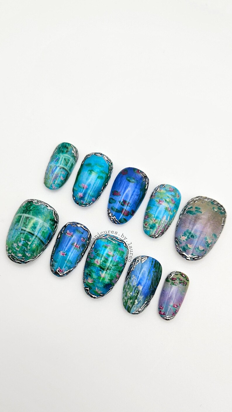 May include: A set of ten artificial nails with a water lily design. The nails are oval-shaped and feature a silver metallic trim. The artwork includes shades of blue, green, and pink, resembling a Monet painting.