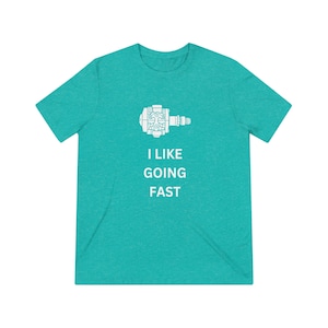 May include: Teal short-sleeve t-shirt with a white graphic of a bicycle pedal and the text "I LIKE GOING FAST". The shirt is made of a soft, comfortable material.