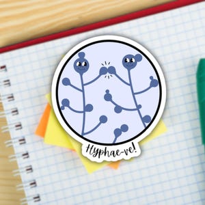 Puede incluir: Una pegatina azul y blanca con dos personajes de hongos de dibujos animados dándose un high five. El texto "Hyphae-ve!" está escrito debajo de los personajes.