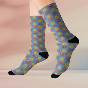 Puede incluir: Calcetines azules con un patrón repetido de frutas amarillas y rojas con caras sonrientes. Los calcetines tienen talones y dedos negros.