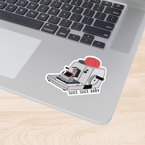 May include: A white sticker featuring a cartoon illustration of a red hat atop a machine with the text "SLICE SLICE BABY" below.