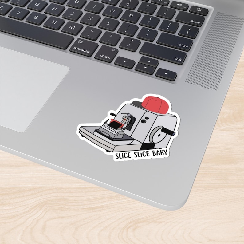 May include: A white sticker featuring a cartoon illustration of a red hat atop a machine with the text "SLICE SLICE BABY" below.