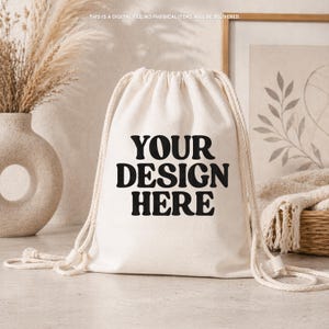 Puede incluir: Una mochila de cordón de color crema hecha de tela con correas de cuerda blanca gruesa. La parte frontal de la bolsa presenta el texto negro "YOUR DESIGN HERE" en una fuente negrita y ondulada. El texto "THIS IS A DIGITAL FILE. NO PHYSICAL ITEMS WILL BE DELIVERED" está impreso en letras blancas pequeñas en la parte superior.
