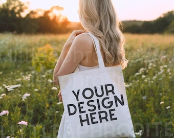 Puede incluir: Una bolsa de mano blanca con el texto "YOUR DESIGN HERE" en negro, sostenida por una persona en un campo de flores. La bolsa tiene correas largas y forma rectangular. El fondo presenta una puesta de sol y el texto "THIS IS A DIGITAL FILE. NO PHYSICAL ITEMS WILL BE DELIVERED."