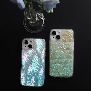 May include: Two iridescent green and white iPhone cases with a mother of pearl design. The cases are on a black surface.