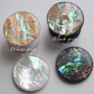 May include: Four iridescent plugs with different colored grips. One plug has a white grip and the text "White grip". Another plug has a black grip and the text "Black grip". The other two plugs are a pearlescent white.
