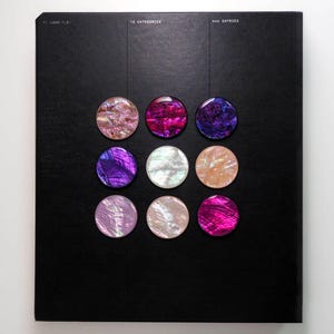May include: A black notebook with nine iridescent, circular embellishments in shades of pink, purple, and white. The top of the notebook has the text "12 CATEGORIES" and "444 ENTRIES".
