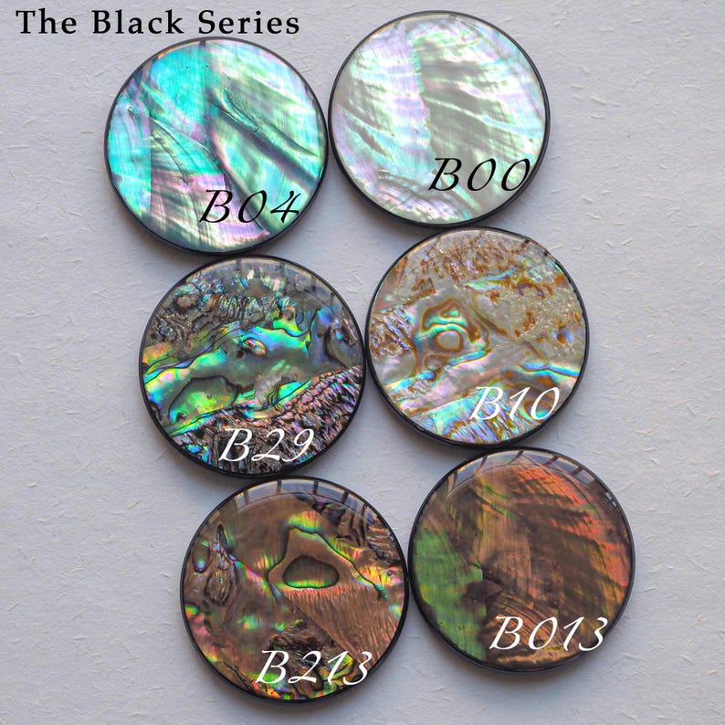 May include: Six round, iridescent abalone shell cabochons in the Black Series. Each cabochon has a unique pattern of colors, including blues, greens, and browns. The text "The Black Series" is at the top.