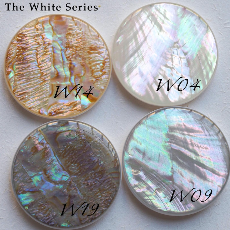 May include: Four round, iridescent mother-of-pearl shell pieces with the text "The White Series". Each piece has a unique pattern and is labeled with a "W" followed by a number: W14, W04, W19, and W09. The shells display a range of colors.