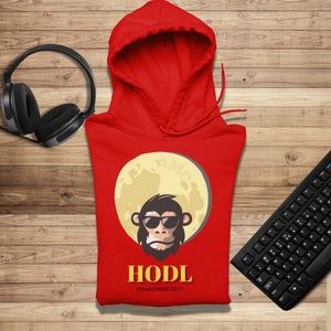 Puede incluir: Sudadera con capucha roja con una luna amarilla y un mono de dibujos animados con gafas de sol. El texto "HODL Established 2021" está impreso debajo de la imagen.