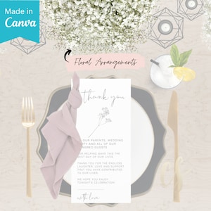 May include: A white card with a thank you message and a small floral illustration. The card is on a table setting with a pink napkin, a gold fork, and a black and gold plate.