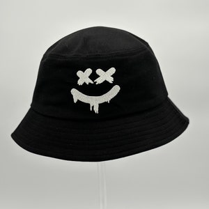 May include: Black bucket hat with a white embroidered smiley face with X's for eyes.