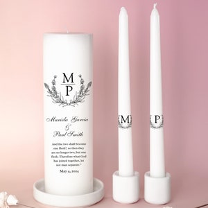 May include: Two white wedding unity candles with black floral designs and the initials "M" and "P" on each. The larger candle has the names "Mariela Garcia & Paul Smith" and the date "May 4, 2024" printed on it. The text "And the two shall become one flesh...so then they are no longer two, but one flesh. Therefore what God has joined together, let not man separate." is also printed on the larger candle.