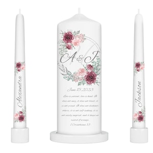 May include: Two white wedding candles with floral designs. The larger candle has a silver circle with the initials A & J and the date June 15, 2023. The text "Love is patient, love is kind. It does not envy, it does not boast, it is not proud. It does not dishonor others, it is not self-seeking, it is not easily angered, and it keeps no record of wrongs. 1 Corinthians 13" is printed on the candle. The smaller candles have the names Alexandra and Jackson printed on them.