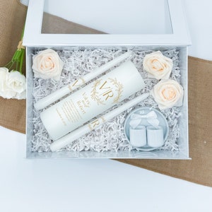 May include: White wedding unity candle set with a gold wreath and the initials VR. The candles are in a white box with white tissue paper and two small white candle holders. The box is surrounded by artificial peach roses.