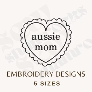 May include: A black and white design featuring a heart-shaped emblem with the words "aussie mom" inside. The heart has a scalloped border. Below, the text reads "EMBROIDERY DESIGNS" and "5 SIZES".
