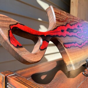 Op de afbeelding: Een houten snijplank met een uniek, abstract ontwerp. De plank is gemaakt van walnoot hout en heeft rode epoxyhars accenten. De plank heeft een handvat en is gevormd als een vis.