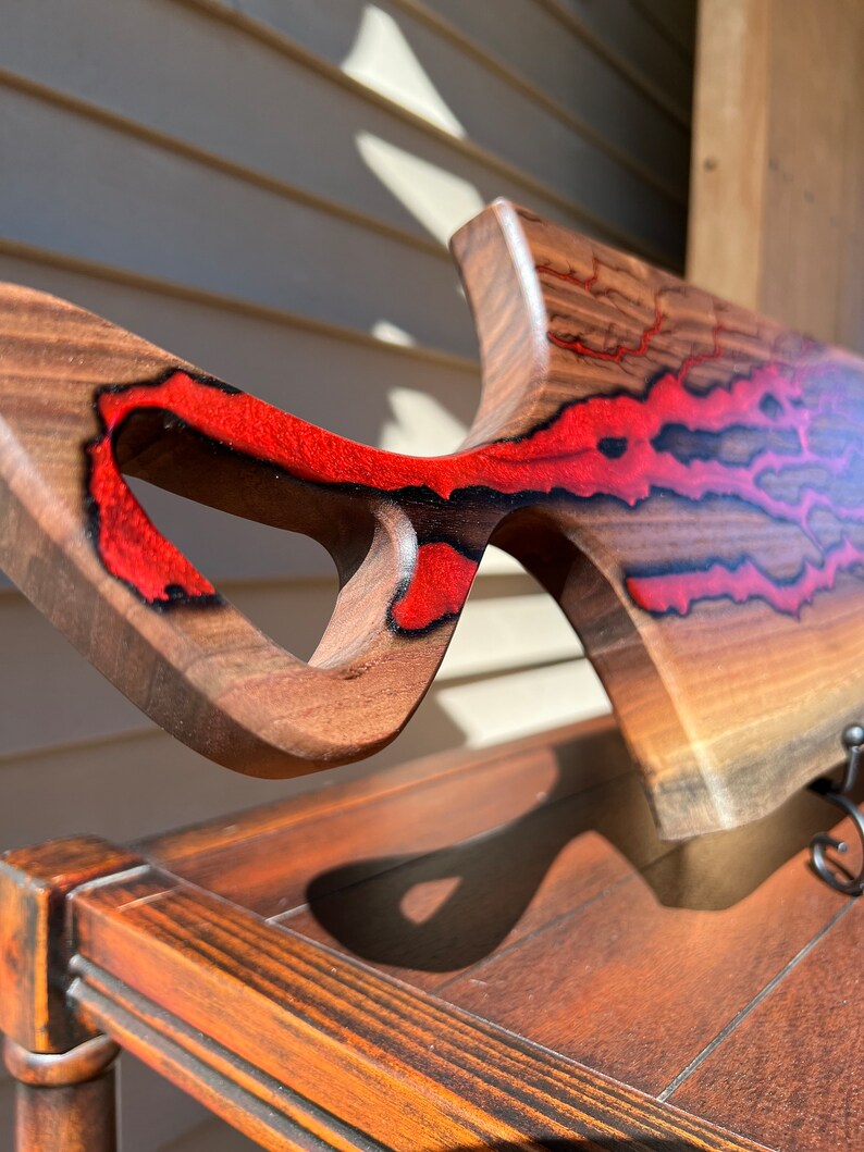 Op de afbeelding: Een houten snijplank met een uniek, abstract ontwerp. De plank is gemaakt van walnoot hout en heeft rode epoxyhars accenten. De plank heeft een handvat en is gevormd als een vis.