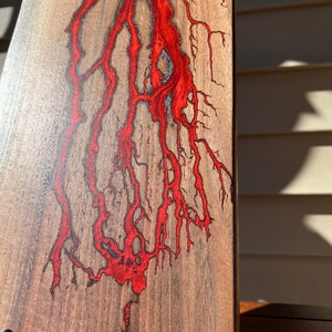 Op de afbeelding: Een houten snijplank met een rood epoxyharsontwerp. De hars stroomt door het hout in een natuurlijk, organisch patroon.