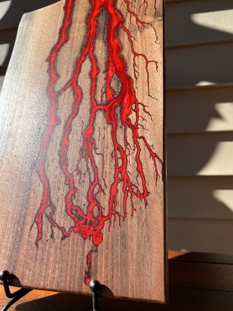 Op de afbeelding: Een houten snijplank met een rood epoxyharsontwerp. De hars stroomt door het hout in een natuurlijk, organisch patroon.