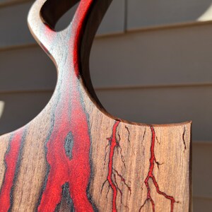 Op de afbeelding: Een houten snijplank met een rood epoxyharsontwerp. De hars stroomt door het hout in een natuurlijk patroon, waardoor een uniek en prachtig stuk ontstaat.
