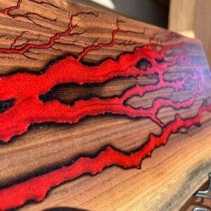 Op de afbeelding: Een houten plank met rood hars dat door de nerf stroomt. Het hars heeft een glinsterende afwerking en cre&euml;ert een uniek patroon.