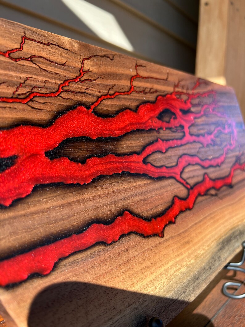 Op de afbeelding: Een houten plank met rood hars dat door de nerf stroomt. Het hars heeft een glinsterende afwerking en cre&euml;ert een uniek patroon.
