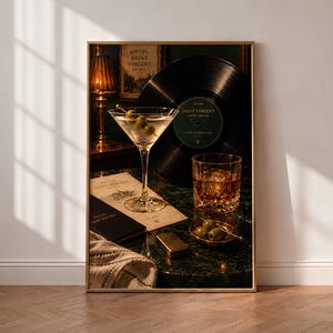 Op de afbeelding: Een ingelijste kunstdruk met een martiniglas met olijven, een vinylplaat met het label Hotel Saint Vincent, een glas whisky met ijs, een schaaltje olijven, een gouden aansteker en een menukaart op een donkergroen marmeren oppervlak.