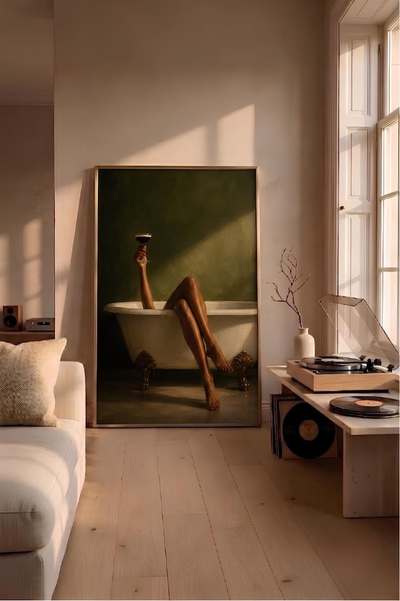 May include: A framed wall art print depicting a person with legs extended out of a white clawfoot bathtub against a dark olive green background. One arm is raised, holding a dark cocktail glass. The artwork is displayed in a living room setting.