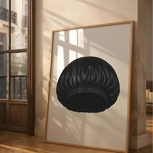 Puede incluir: Impresión enmarcada de un gorro de satén negro. El gorro tiene una corona redonda y una banda en la base. La obra de arte se exhibe sobre un fondo claro, apoyada contra una pared en una habitación con suelo de madera.