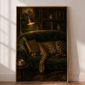 May include: A framed wall art print depicting a leopard resting on a dark green velvet sofa with a book covering its face. The scene includes a lit brass desk lamp, a bookshelf in the background, and a small side table with a cup of coffee.