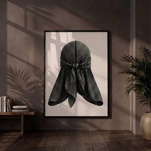 May include: A framed wall art print featuring a black durag covered in small, reflective silver studs. The durag is depicted with a central knot and two hanging ties, set against a plain white background within a thin black frame.