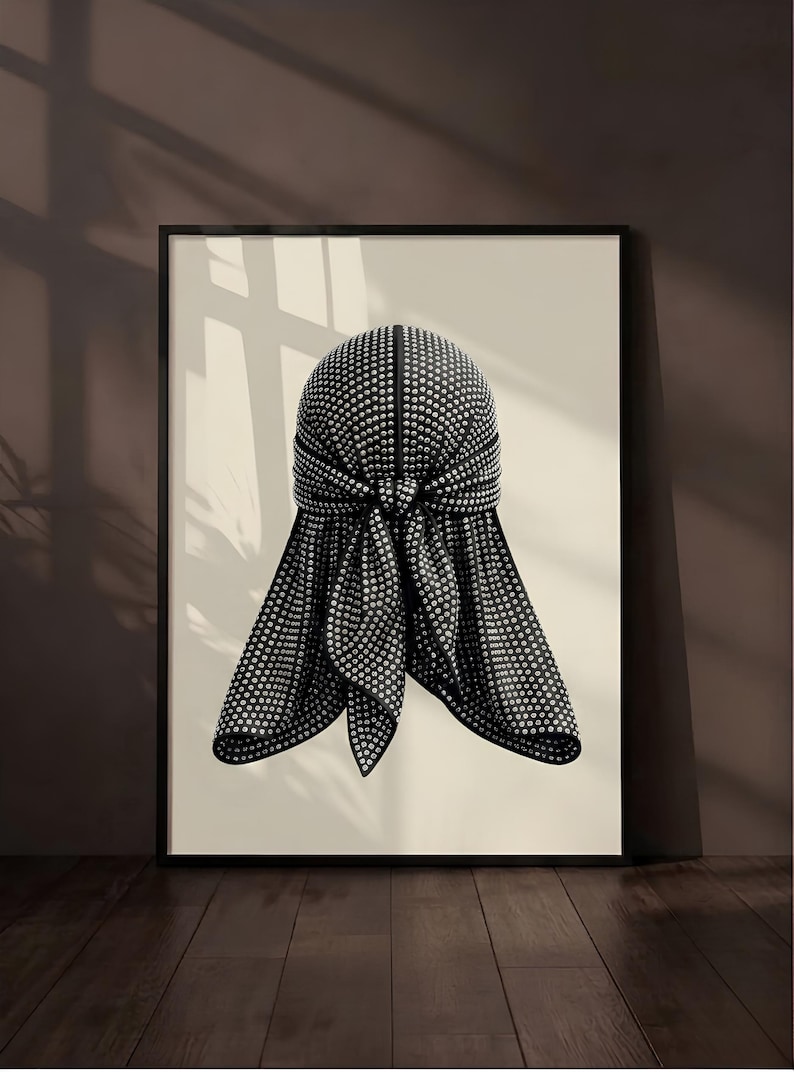 May include: A framed wall art print featuring a black durag covered in small, reflective silver studs. The durag is tied in the center with two long tails hanging down, displayed against a solid light beige background within a thin black frame.