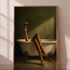 May include: A framed wall art print depicting a white clawfoot bathtub with gold-toned feet against a dark olive green wall. A pair of legs and an arm holding a stemmed cocktail glass are visible, with light casting a diagonal shadow across the scene.