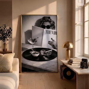 May include: A framed black and white wall art print featuring a person wearing sunglasses reading a magazine titled THE VIBE, with a martini glass, a small bowl of olives, and a glass ashtray with a cigarette resting on a vinyl record.