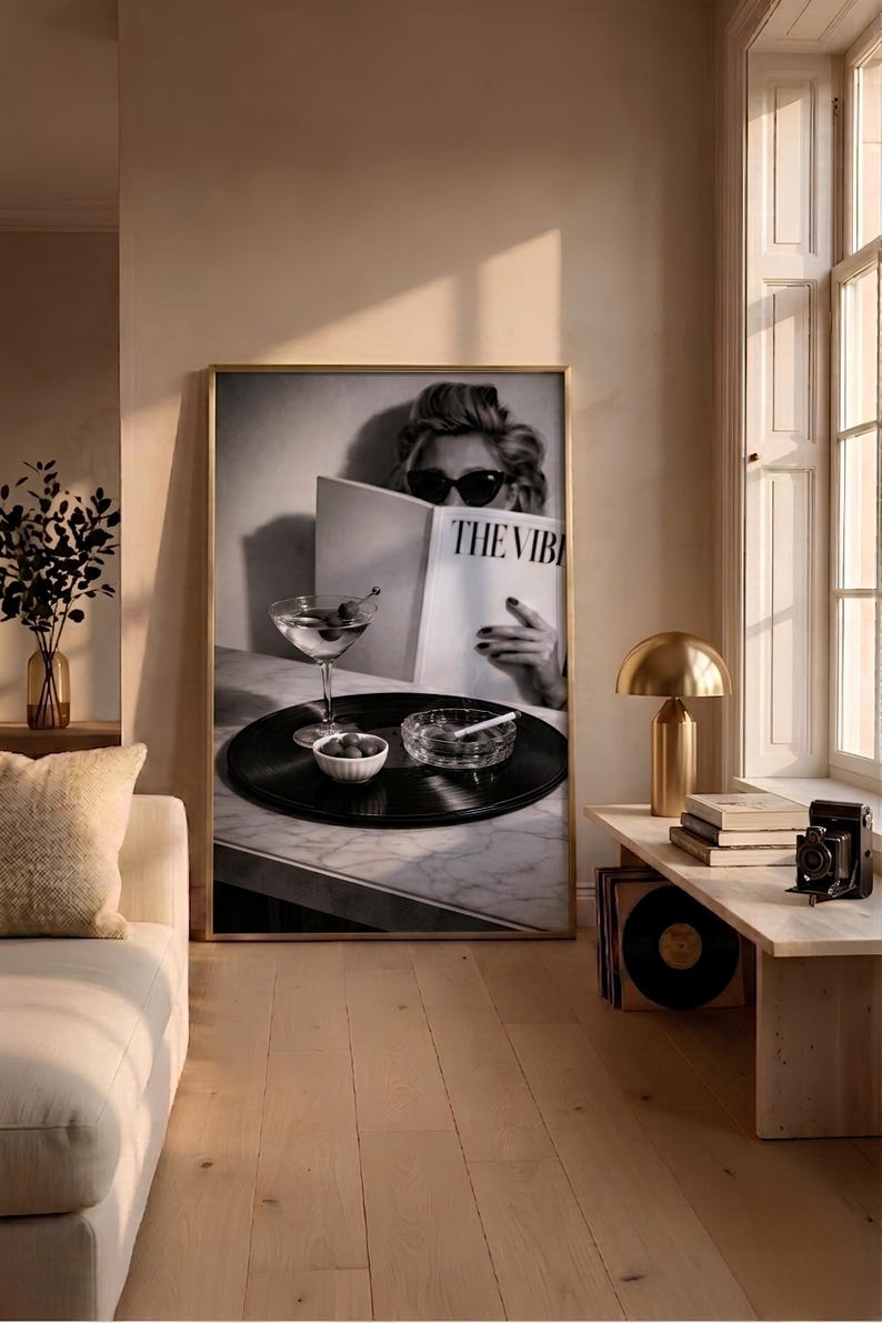 May include: A framed black and white wall art print featuring a person wearing sunglasses reading a magazine titled THE VIBE, with a martini glass, a small bowl of olives, and a glass ashtray with a cigarette resting on a vinyl record.