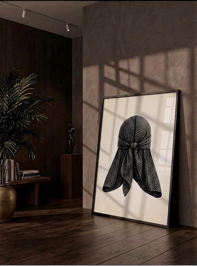 May include: A framed wall art print featuring a black durag with a white polka dot pattern. The durag is depicted with a central knot and two hanging ties, centered on a light cream background within a thin black frame.