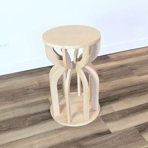 May include: A light-colored wooden stool with a round seat and a unique, open-legged base. The stool's design features curved supports that connect the seat to a circular base. The wood has a natural, unfinished appearance, and the stool is set against a white wall.