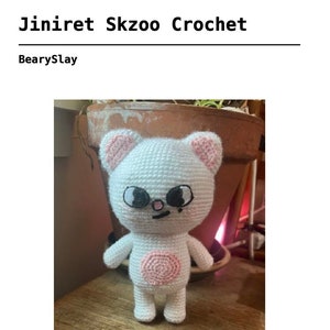 May include: White crocheted plush toy in the shape of a bear with pink ears, a pink circle on its belly, and black eyes. The bear has a small black nose and a black mouth.