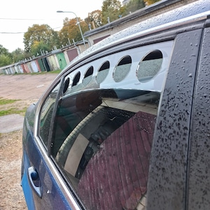 May include: A blue car with a custom window vent kit. The vent kit has a series of round holes cut into a metal panel.
