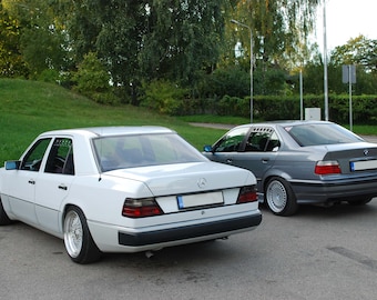 May include: A white Mercedes-Benz sedan parked next to a gray BMW sedan. Both cars are parked on a paved surface.