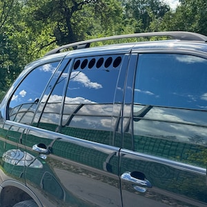 May include: Black SUV with a custom window vent with a row of circular cutouts. The vent is on the rear passenger side door.