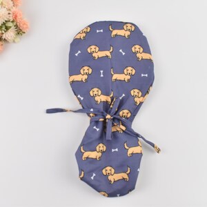 May include: A blue surgical scrub cap featuring a repeating pattern of tan dachshund dogs and white bone shapes. The cap has a tie closure and is designed for medical professionals or pet lovers.