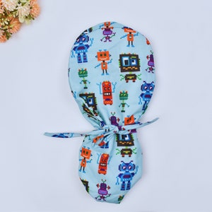 May include: A light blue surgical scrub hat with a pattern of colorful pixelated robots. The hat has a tie at the back.