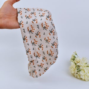 Puede incluir: Un gorro de ducha de tela de color crema con un estampado floral de pequeñas flores naranjas y hojas verdes.