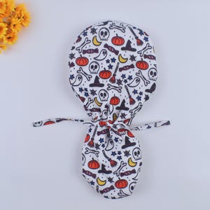 May include: White scrub hat with a Halloween themed print featuring ghosts, pumpkins, skulls, bones, stars, candy, witches hats, and broomsticks.