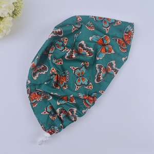 May include: A teal blue surgical scrub hat with a colorful butterfly print. The hat has a white drawstring and a white button.